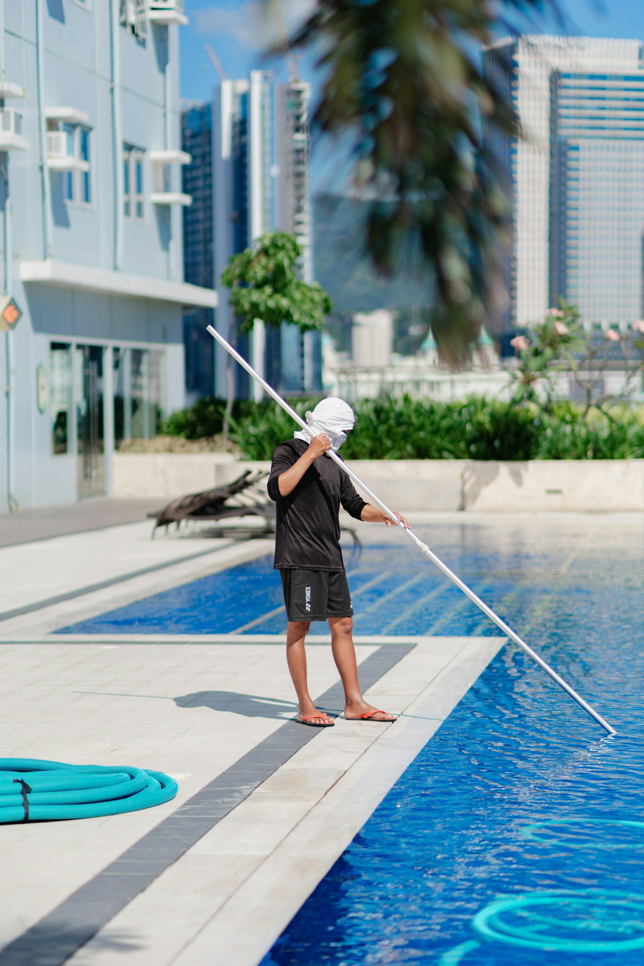 Pool technician cleaning a bright blue swimming pool with a long service pole